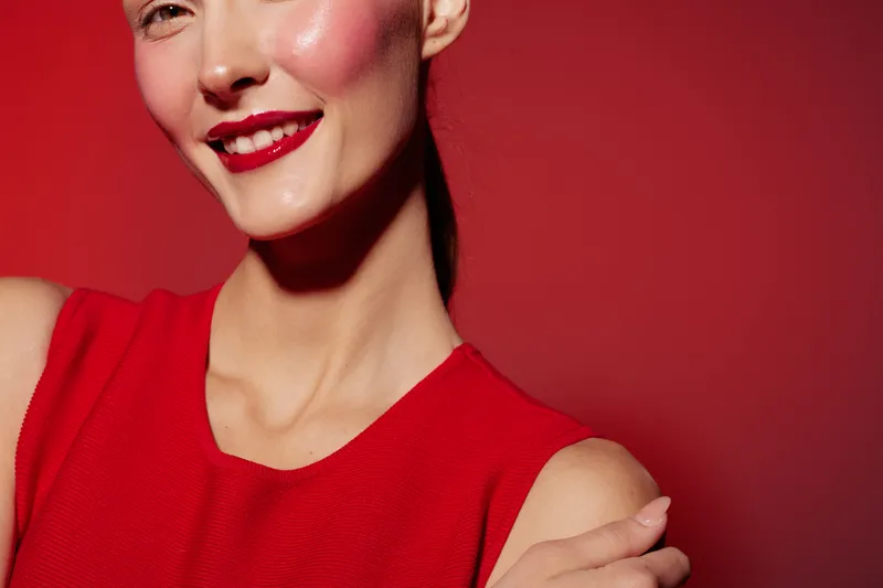 Close-up of smiling woman with red lipstick and red dress on red background. Concept of beauty, fashion, makeup, and confident female portrait with vibrant colors and studio lighting.