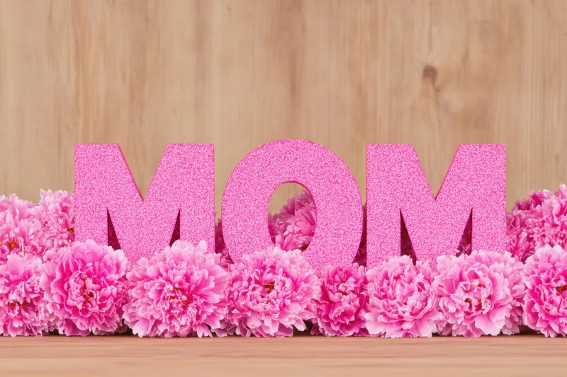Ярко-розовые буквы «MOM» в окружении розовых цветов создают трогательную сцену ко Дню матери