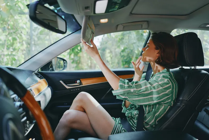 Woman sits in a car seat applying lipstick, capturing a candid beauty moment inside a stylish vehicle.