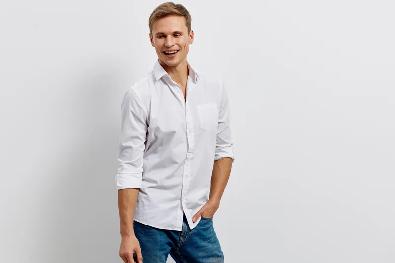 Smiling man wearing casual white shirt and blue jeans looking at camera on plain gray background studio portrait. People lifestyle concept