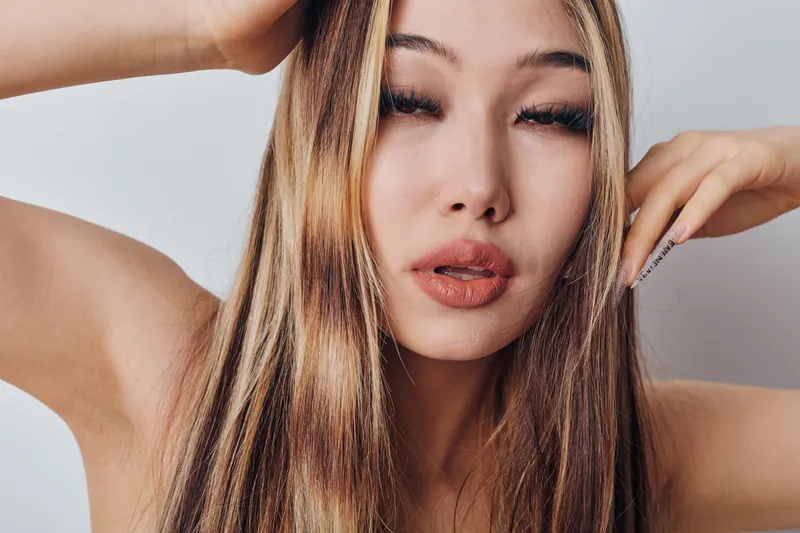 Closeup portrait of young woman with long hair posing with hand on face and eyes almost closed for beauty, fashion and skincare concept in studio lighting.