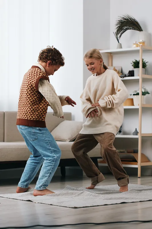 Authentic moment of children at home, showing playful activity and a school inspired lifestyle. Two friends dance in a cozy living room, reflecting genuine joy and natural spontaneity.