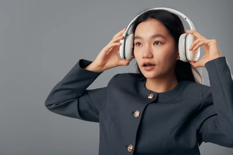 Young woman wearing headphones posing on gray background, listening to music or podcast, casual style with dark jacket, lifestyle and technology concept for audio entertainment and communication.