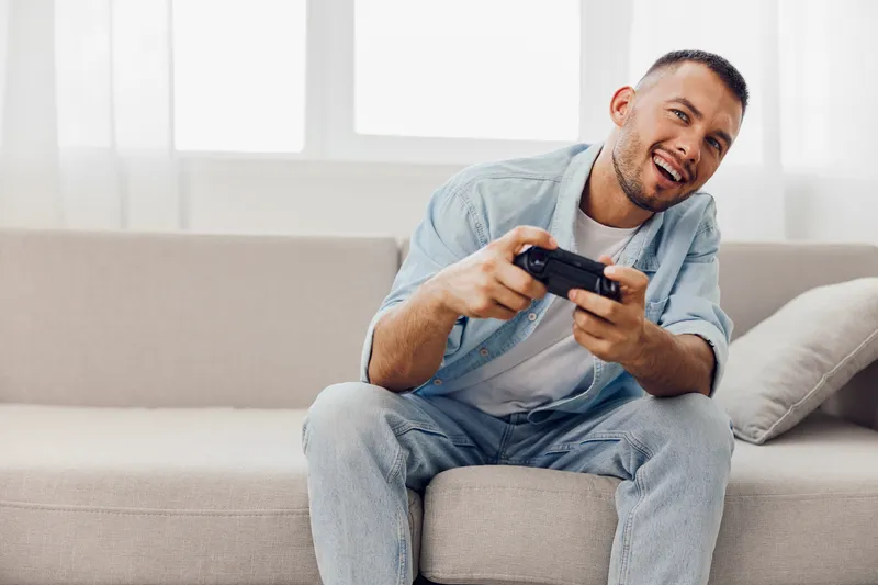 A joyful man playing video games at home, embracing a moment of relaxation and self-care amidst personal challenges and digital distractions.