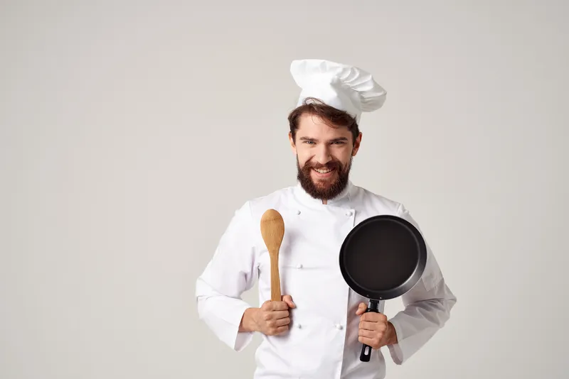 Весёлый шеф-повар мужского пола работает на кухне, занимаясь приготовлением пищи профессионально