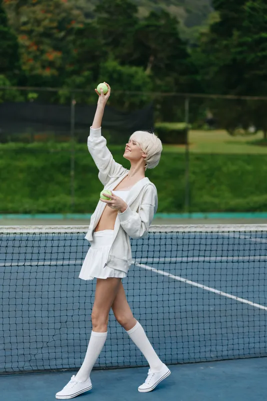 Stylish young model playing tennis in a fashionable outfit with a confident expression, surrounded by a vibrant green background in a sunny sports setting