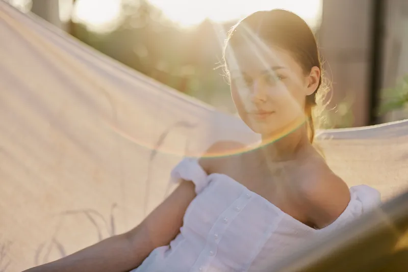 Beautiful woman in a white dress relaxing in a hammock during sunset, showcasing serene emotions in an outdoor setting with soft sunlight