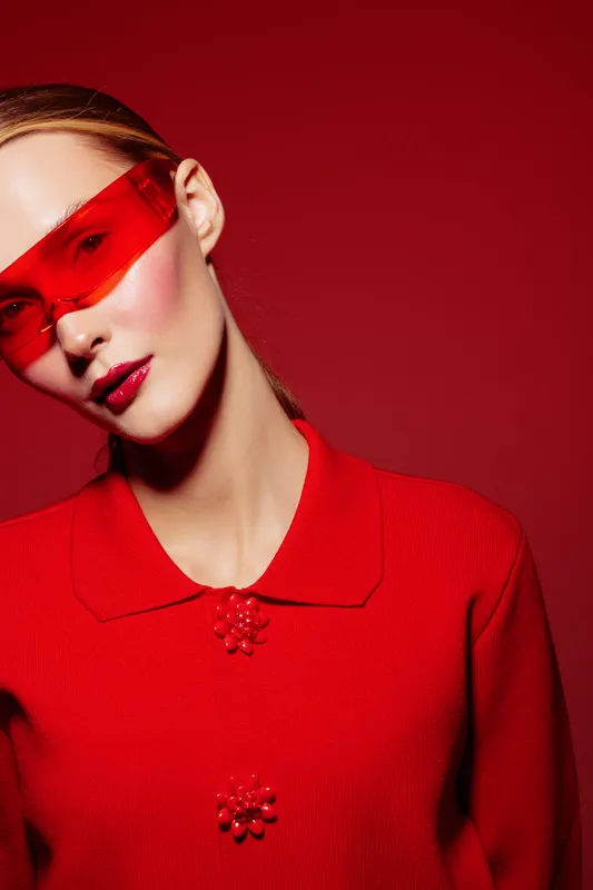 Portrait of a stylish woman wearing red sunglasses and a red sweater against a red background. Fashion concept with bold colors and modern accessories in a studio setting.