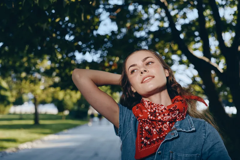 Lifestyle woman in modern boho-western denim street style with red bandana enjoying sunny day outdoors, film color tones capturing casual urban fashion vibe.