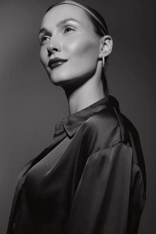 Portrait of a fair skinned Caucasian woman wearing earrings and a satin blouse looking confidently in monochrome lighting.