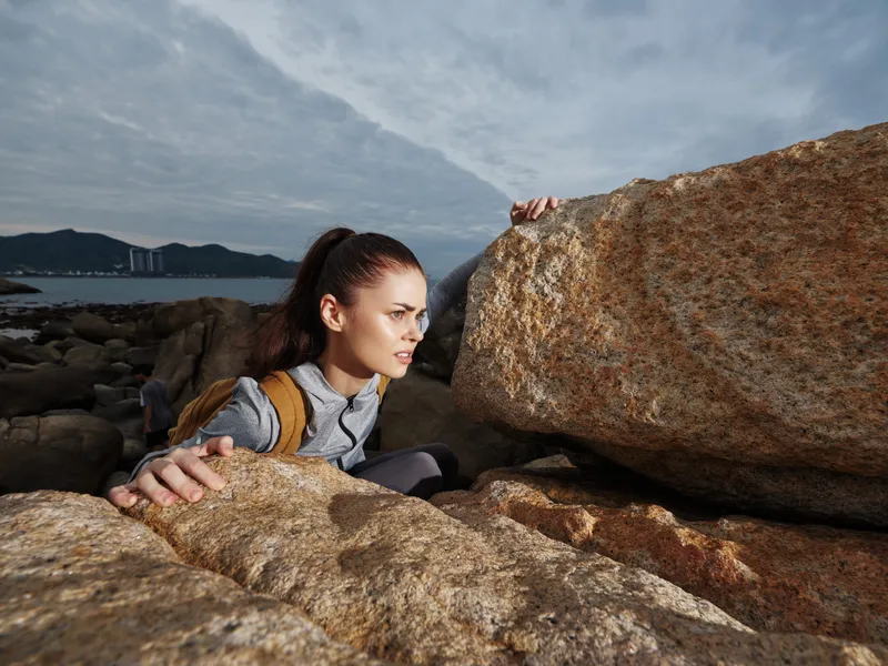 Determined female climber navigating rocky terrain, showcasing adventure and resilience against a dramatic sky backdrop