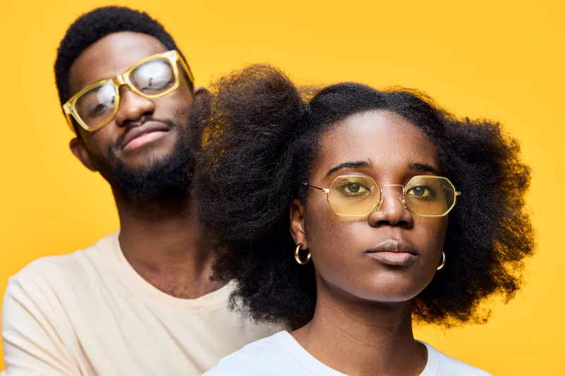 Young Black couple with stylish eyewear, showcasing confidence and individuality against a vibrant yellow background, perfect for lifestyle and fashion themes
