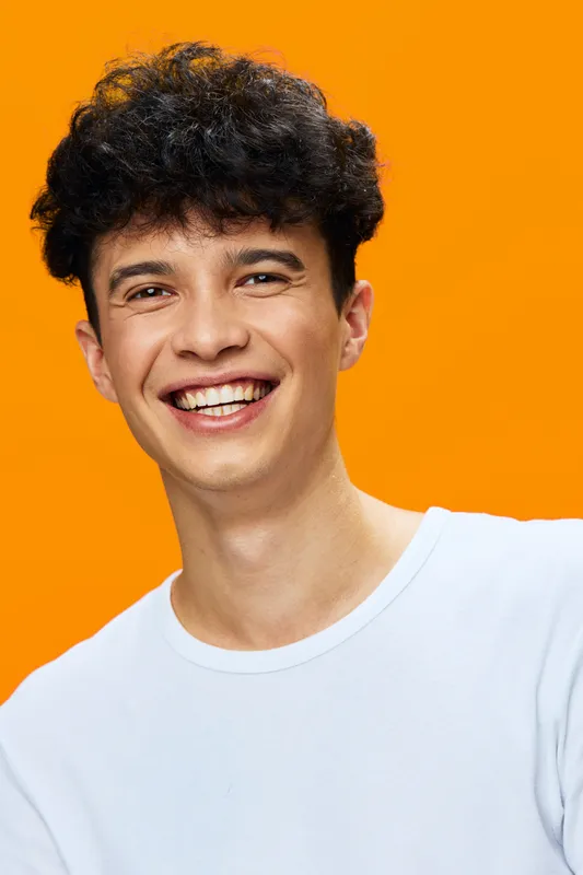 smiling young man with curly hair wearing white t-shirt on bright orange background, cheerful expression, casual style, studio portrait, vibrant colors