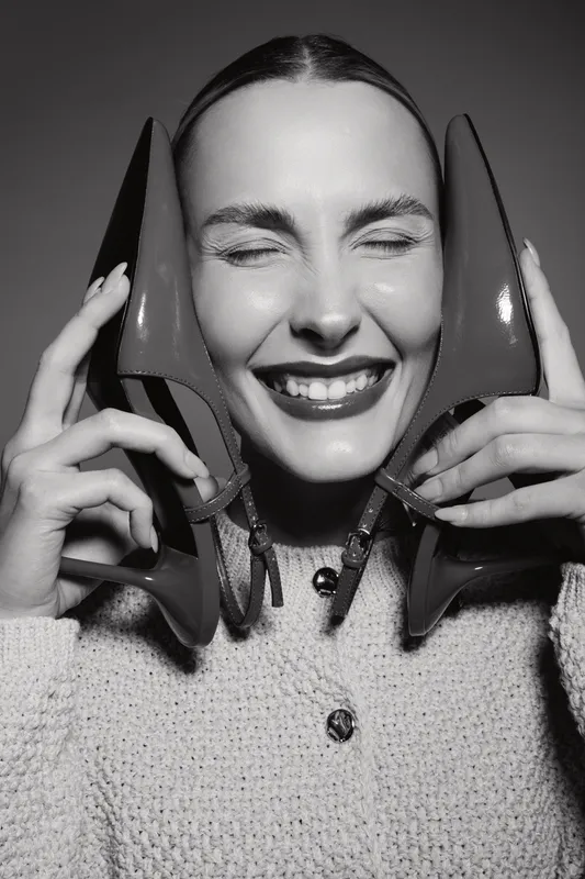Happy Caucasian woman with fair skin holds two high heel shoes near face, eyes closed and smiling. Concept of fashion, joy, lifestyle and beauty portrait.
