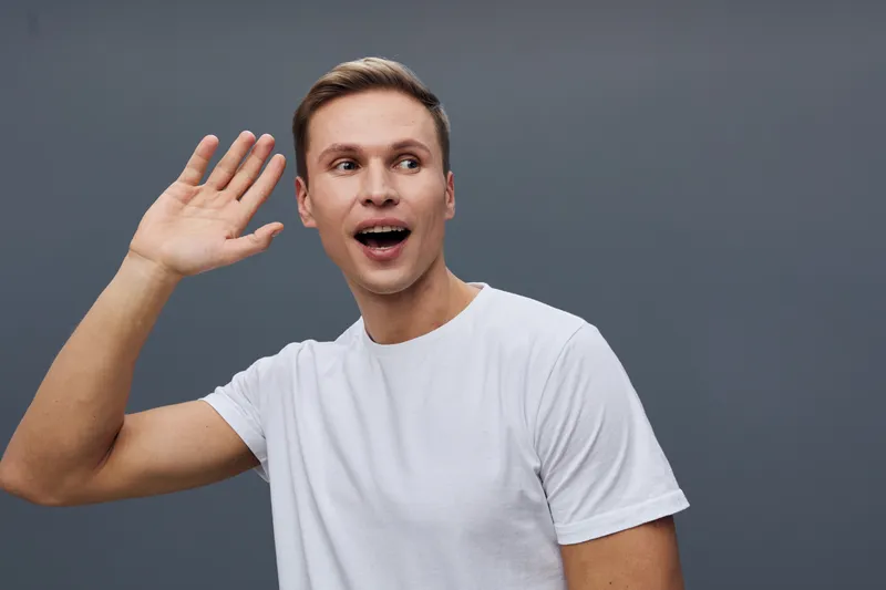 happy young caucasian man wear white t-shirt listen with hand near ear front dark gray background studio portrait digital detox mental health concept
