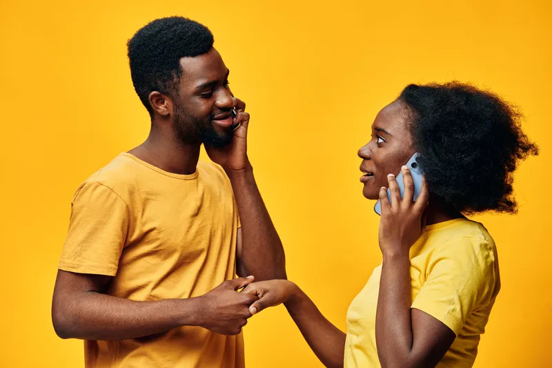Happy couple talking on mobile phones against a bright yellow background, showcasing joy, connection, and communication in modern relationships