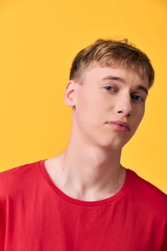 Young adult male in a red shirt against a bold yellow background, casual studio fashion shot with confident expression and clean, minimal composition, ideal for lifestyle and contemporary imagery
