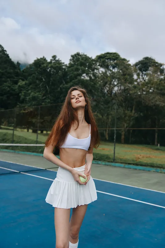 Young athletic woman in a white sports outfit, exuding confidence on a tennis court, showcasing healthy lifestyle and fitness enthusiasm