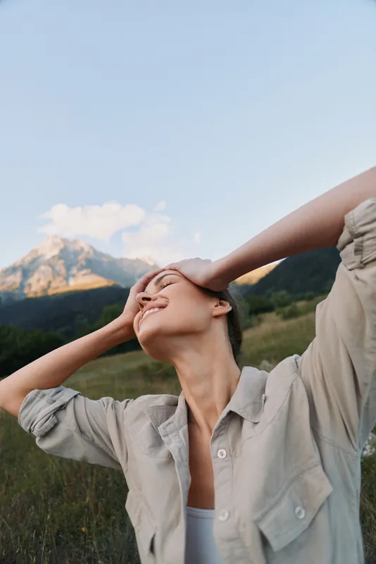 Young woman with relaxed posture outdoors stands in a field with mountains in the background