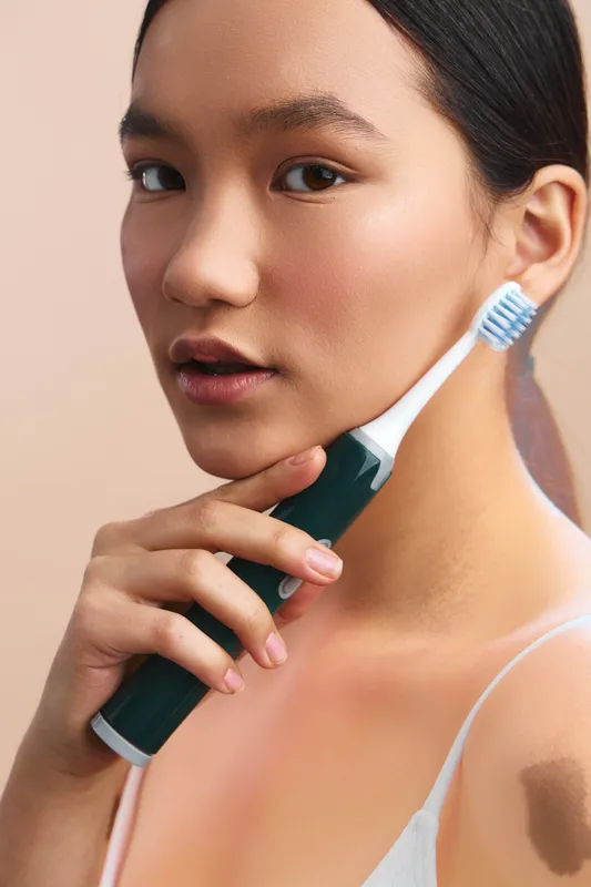 asian woman brushes teeth with an electric toothbrush in a clean bathroom, presenting a calm morning routine. The closeup captures a fresh, healthy vibe and personal care.