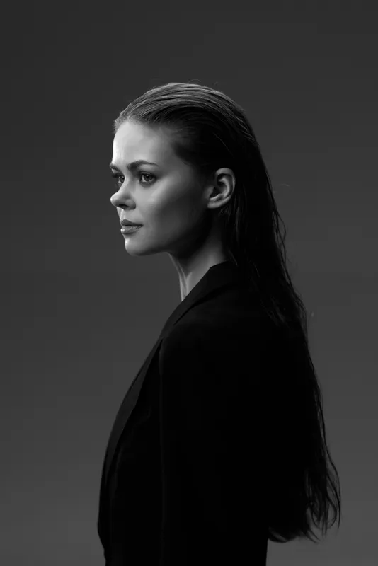 Black and white portrait of a serious woman with long wet hair in dark clothing against gray background