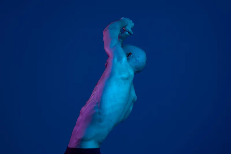 Dynamic man posing dramatically against a blue background, showcasing strength and emotion with striking lighting effects highlighting his form and silhouette.