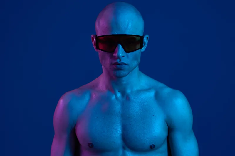 Athletic man wearing sunglasses on a blue background, showcasing a striking blue tone. The image captures a modern and stylish aesthetic, emphasizing confidence and strength.