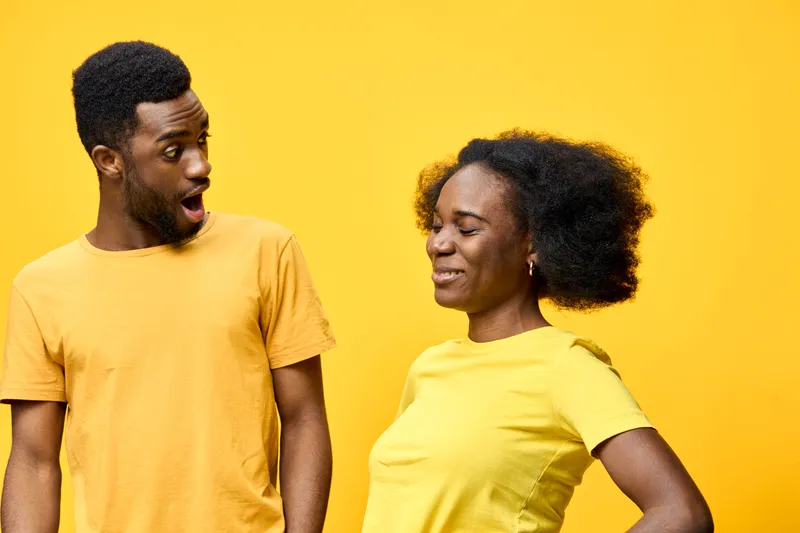 Joyful couple enjoying playful moments together, wearing matching yellow shirts against a vibrant yellow backdrop, expressing surprise and happiness in a lively setting