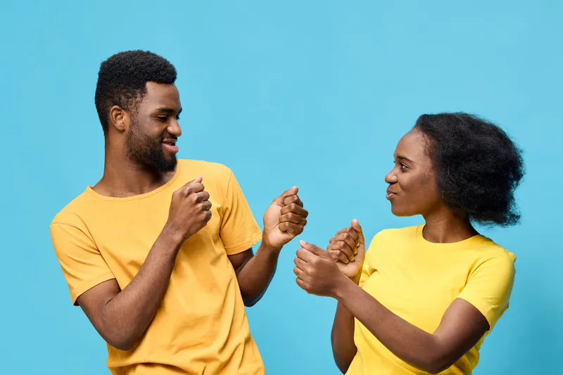 Young African couple smiling and dancing together in vibrant yellow outfits against a bright blue background, showcasing joy and connection in a lively atmosphere