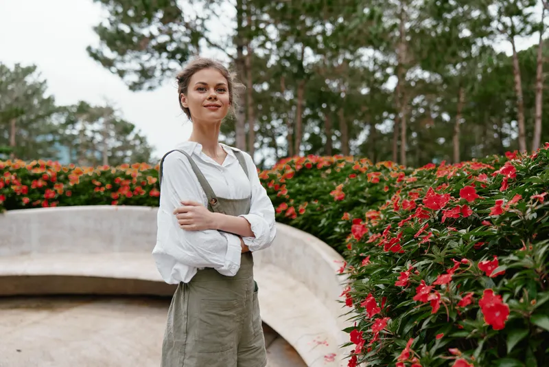 Young woman in casual attire stands confidently amidst vibrant flowers in a serene garden, showcasing a blend of nature and fashion