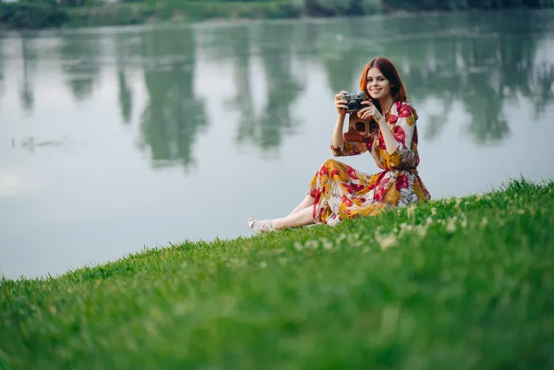 Женщина в платье с фотоаппаратом на природе, делающая снимки — хобби