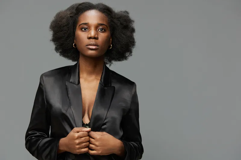 Elegant black woman in a silky blazer, showcasing confidence and beauty against a gray background, representing empowerment and fashion