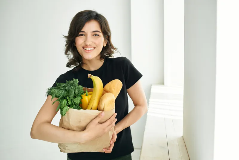 Жизнерадостная брюнетка с пакетом продуктов, здоровое питание, доставка овощей