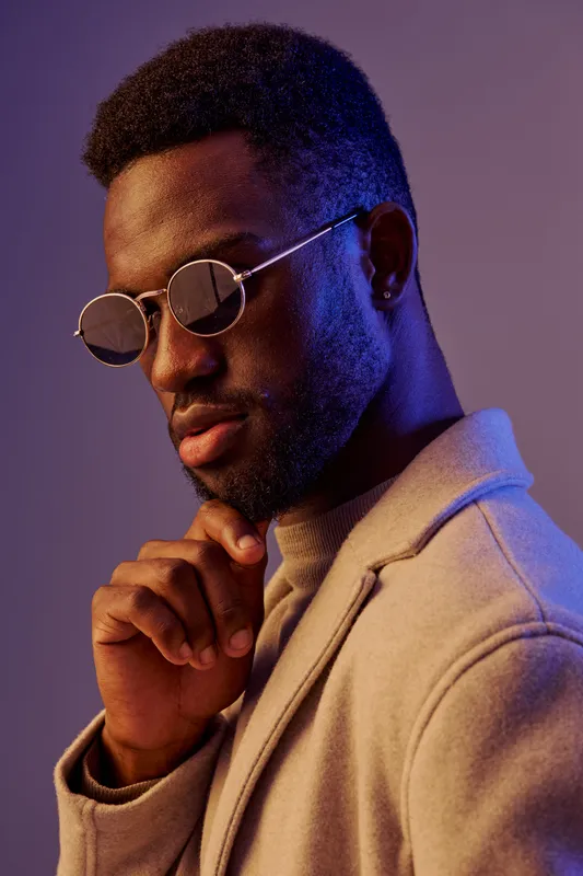 Portrait of a stylish African man in sunglasses, exuding confidence against a vibrant purple backdrop, perfect for fashion and lifestyle imagery