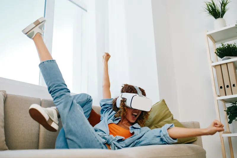 Блаженство виртуальной реальности: радостная женщина в футуристических VR-очках наслаждается кибер-игрой дома