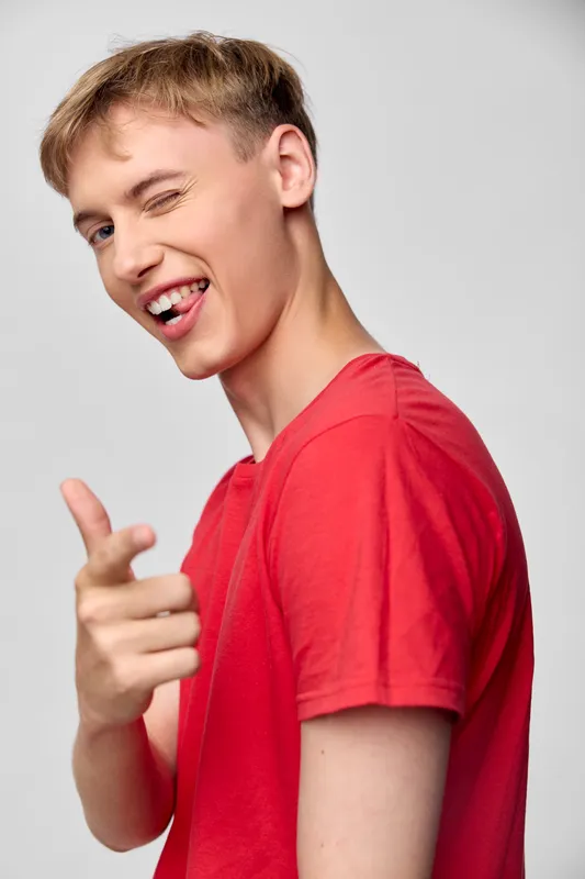 Young man in a red shirt makes a playful wink and pointing gesture, conveying confidence, humor, and energy for lifestyle, youth branding, and casual advertising for social media