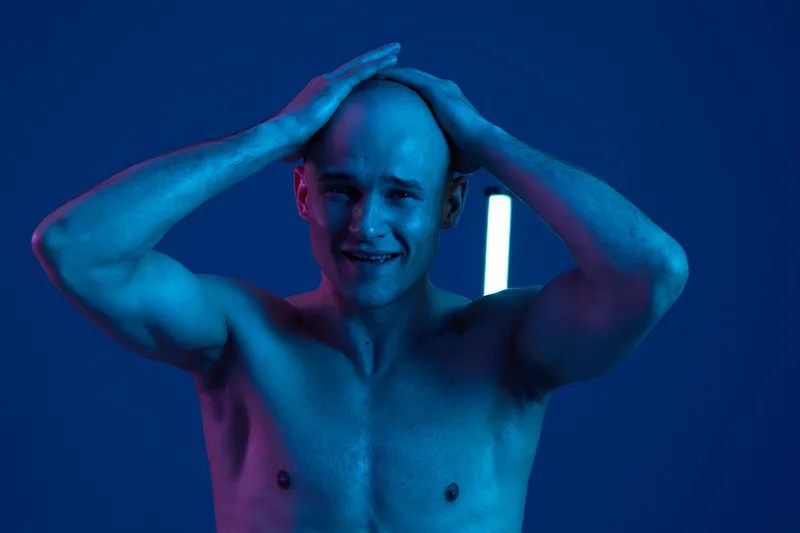 A distressed man expressing intense emotions against a dark blue background with vibrant lighting. This black and white image captures feelings of anguish and despair.