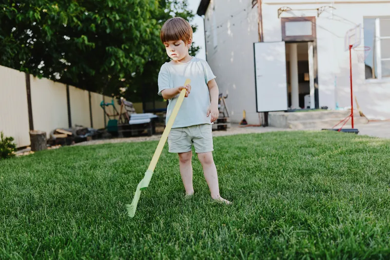 Young boy playing in the garden, exploring nature with curiosity and joy while using a yellow gardening tool to engage with his environment.
