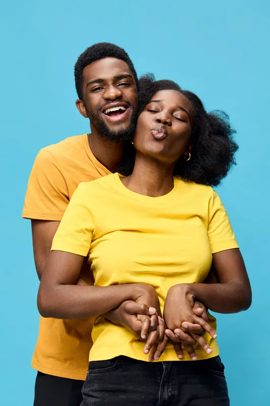 Happy young couple embracing and smiling against a bright blue background, showcasing love and connection, wearing casual yellow and orange t shirts