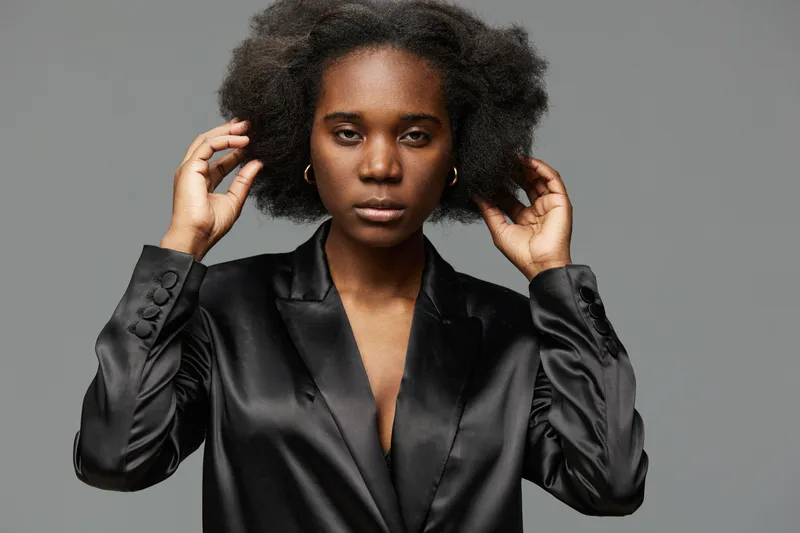 Confident young woman with natural hair in a black satin blazer expressing self acceptance, ideal for concepts of beauty and empowerment