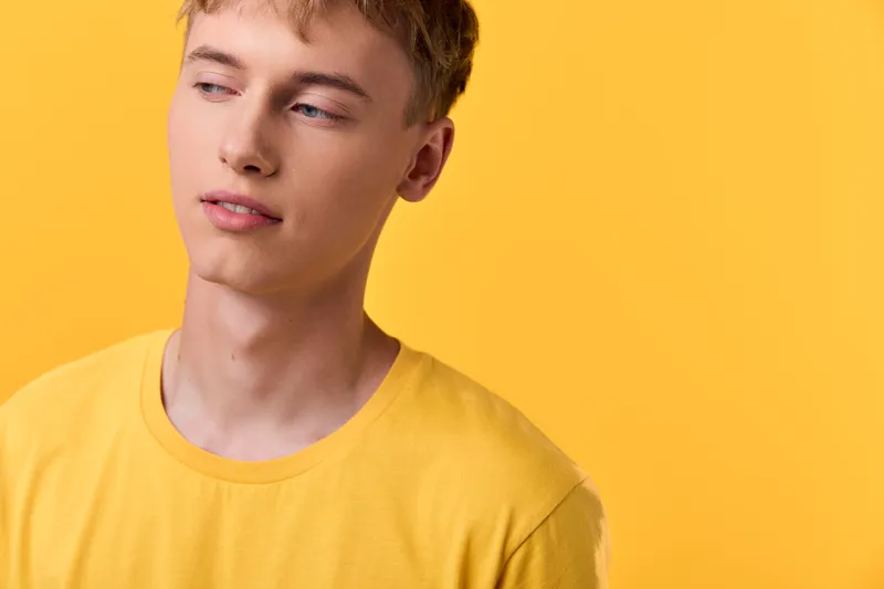 Young man in a yellow shirt against a bright yellow backdrop, conveying casual mood, thoughtful expression and clean lifestyle vibe for fashion imagery, studio style
