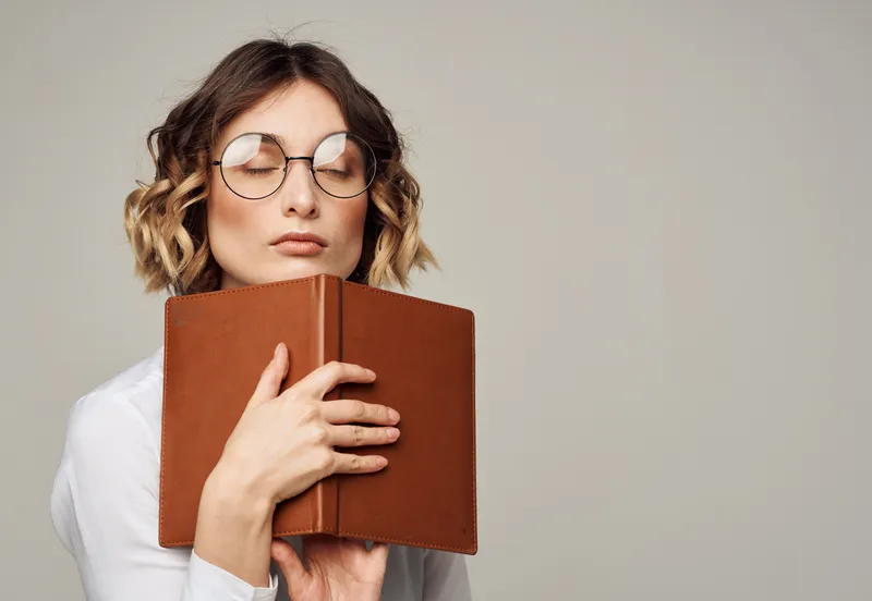 Женщина в очках держит в руке книгу на сером фоне
