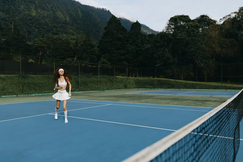 Young woman enjoying a game of tennis on a sunny day, wearing a stylish white sports outfit, exuding joy and enthusiasm