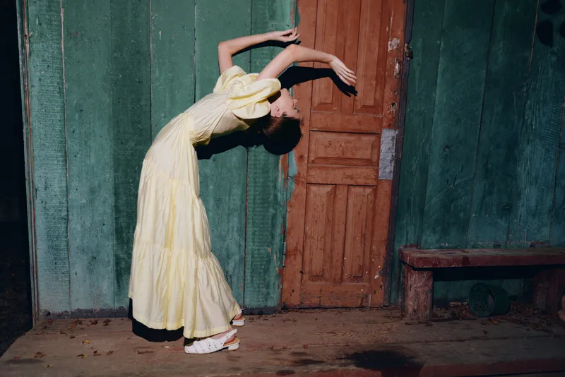 woman dress pose door wall vintage night street, yellow gown arching back by wooden door rustic wall at dusk authenticity inclusivity