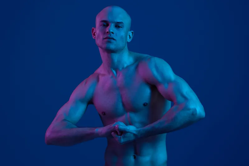 Athletic man posing dramatically in vibrant purple and blue lighting, showcasing a powerful physique and strong emotions. Perfect for fitness and artistic themes.