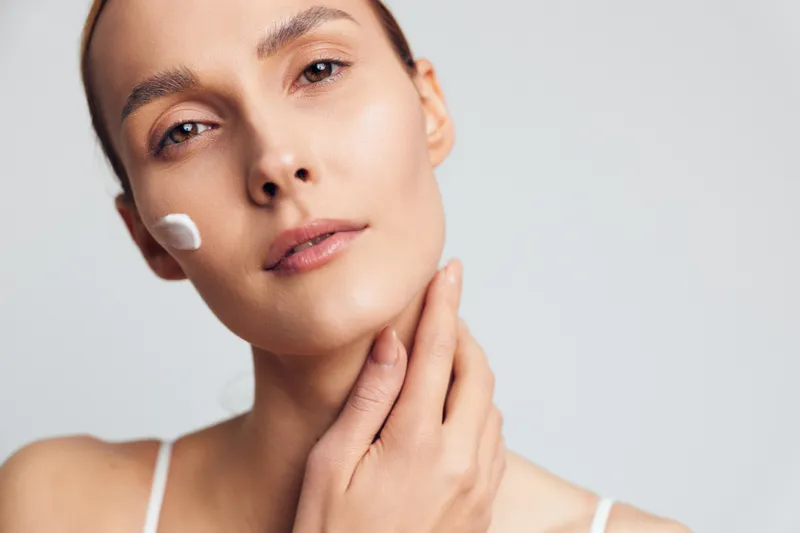 Closeup portrait of woman applying skincare cream on face with gentle hand touch, natural makeup, soft lighting, clean background, healthy skin care routine concept
