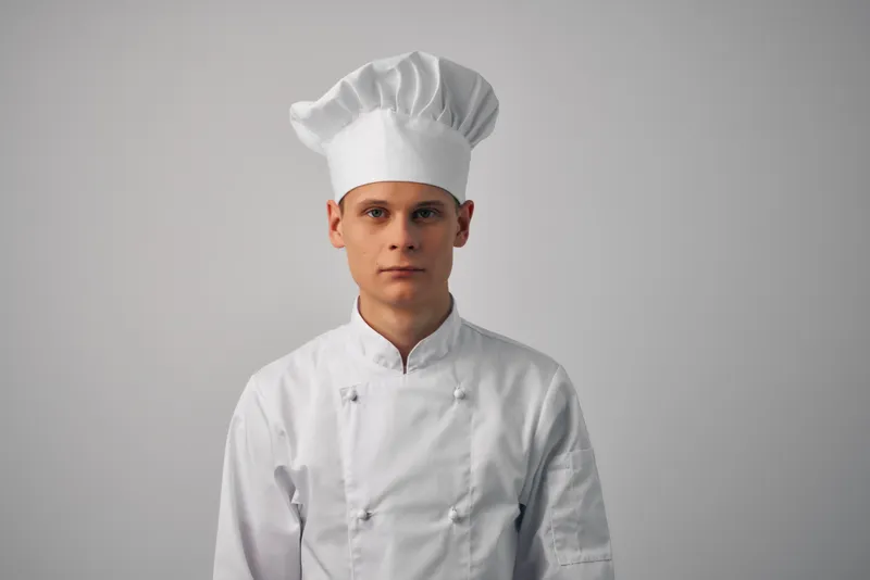Весёлый шеф-повар мужского пола работает на кухне ресторана, занимаясь приготовлением блюд