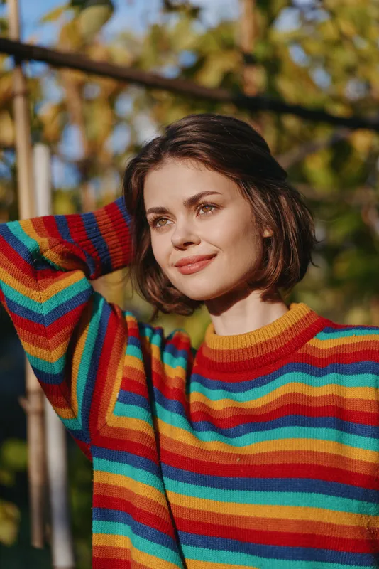 woman portrait smiling in a colorful striped sweater outdoors in autumn sunlight, short hair, closeup headshot with natural light, casual cozy knitwear, relaxed candid lifestyle mood