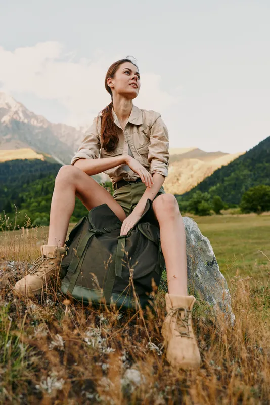 Woman lifestyle outdoor hiking on a mountains landscape with backpack boots, calm expression, natural light, rugged field setting, preparing for adventure in nature