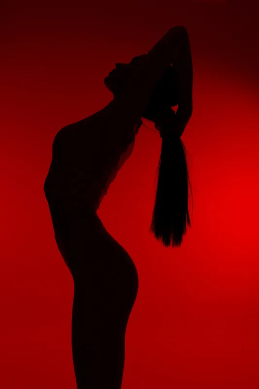 Silhouette of a woman sport fitness posing stretching with long hair tied back against vibrant red background, showcasing flexibility and strength in dynamic workout concept.